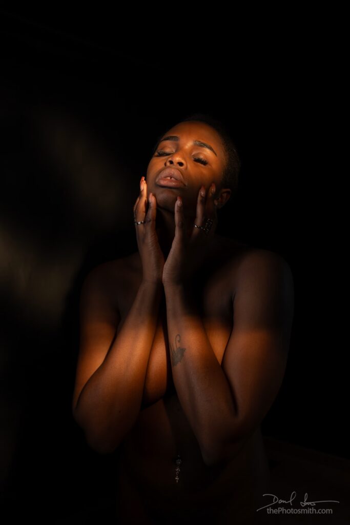 Nude African woman bathed in orange light with her hands to her face