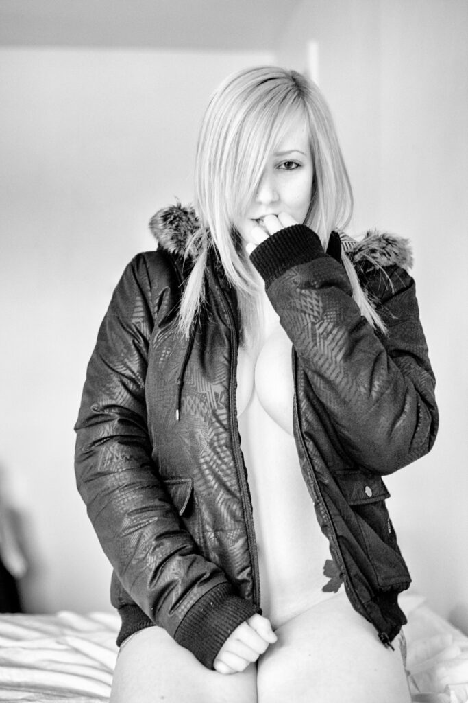 Black and white boudoir photo of a blonde woman wearing a parka and a smile.